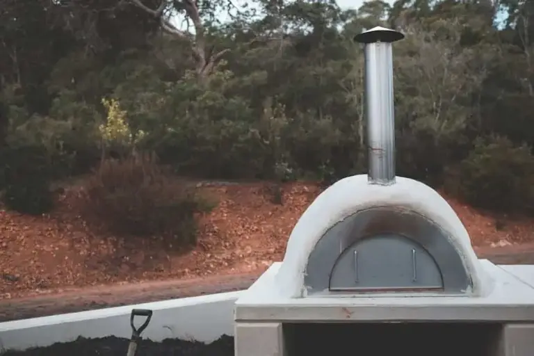 Igloo-style pizza oven finished in white stucco, with a steel chimney pipe, on a concrete block stand