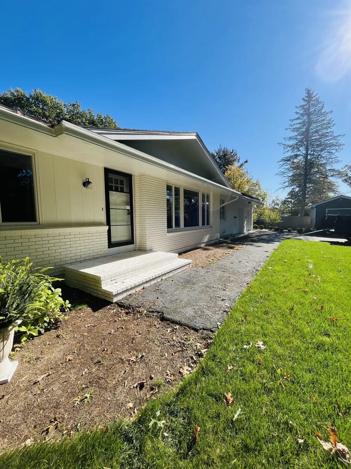 Ranch house front entry before the work, with a single white concrete step and a worn path along the house